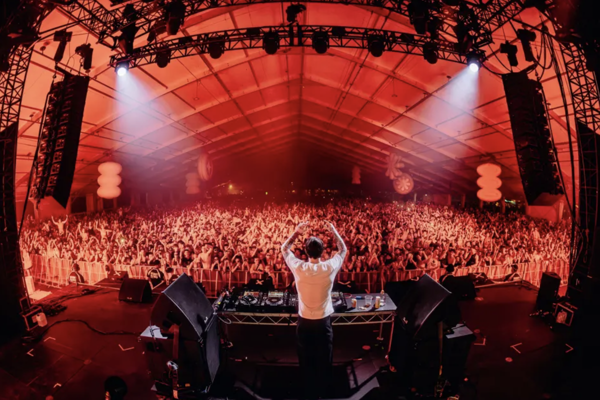 DJ performing on stage at Wildlands Festival looking out over a packed indoor venue crowd bathed in bright red lighting.